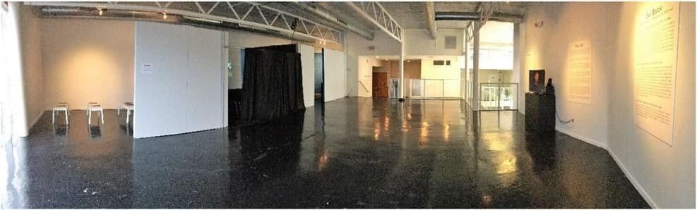 Figure 5 Panoramic view of the Sandra Bland exhibit. To the far left is the memorial space. Next is the dash cam room with the curtain to dim the setting; to the curtain’s right is a partition that makes the living room area of the exhibit. The handrail at the exhibit’s entrance is visible in the background. To the right is the television flanked by three wall plaques. The day I took this photo the chairs had not yet been set out and arranged. Author photo.